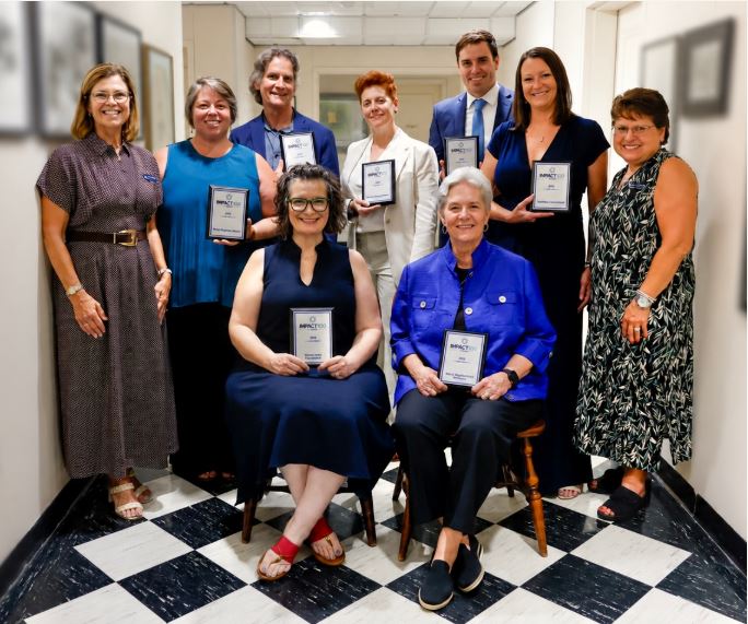 A group of diverse women smiling and posing together closely, representing community connection and collective giving at an Impact 100 event.
